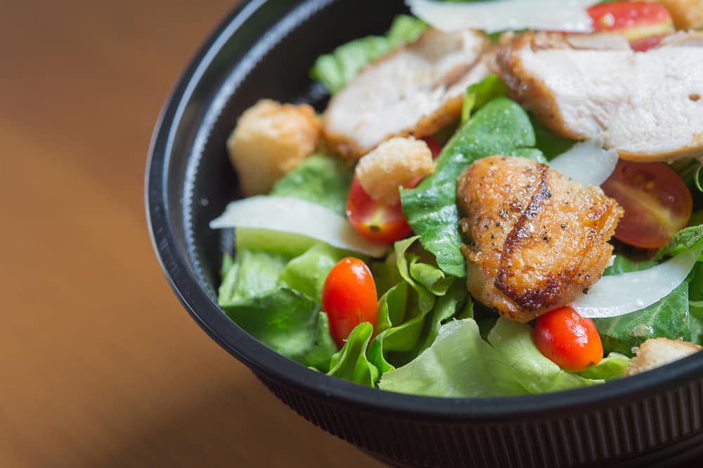 Plastic black bowl filled with chicken salad on a wooden table. 