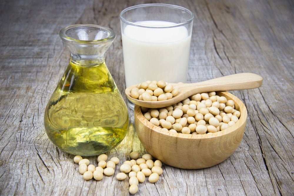 A glass of soy milk with some ingredients in the foreground sitting on a wooden table. 