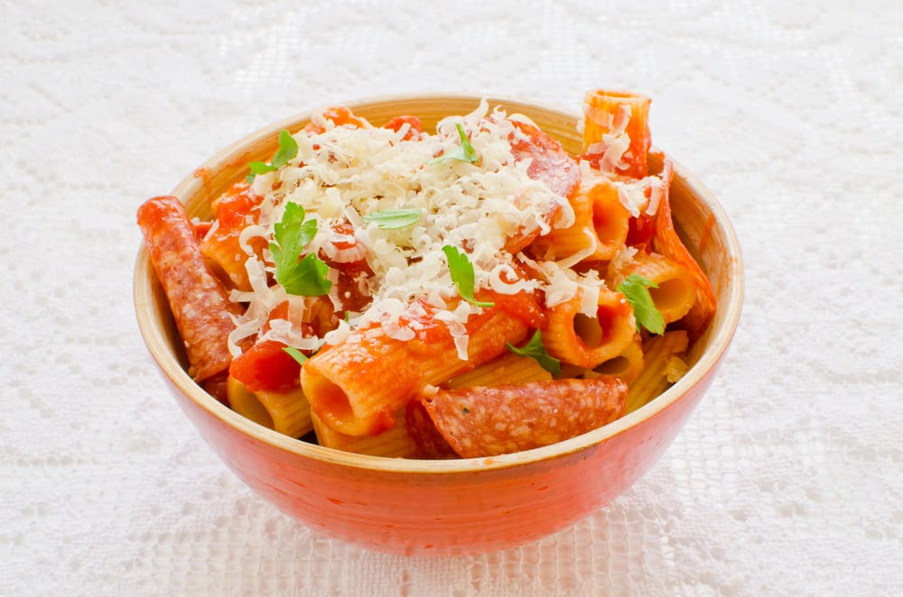 A bowl of pasta with pepperoni topped with grated cheese.