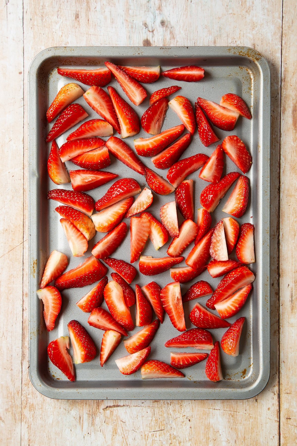 Strawberries sliced into quarters on a non-stick tray. 