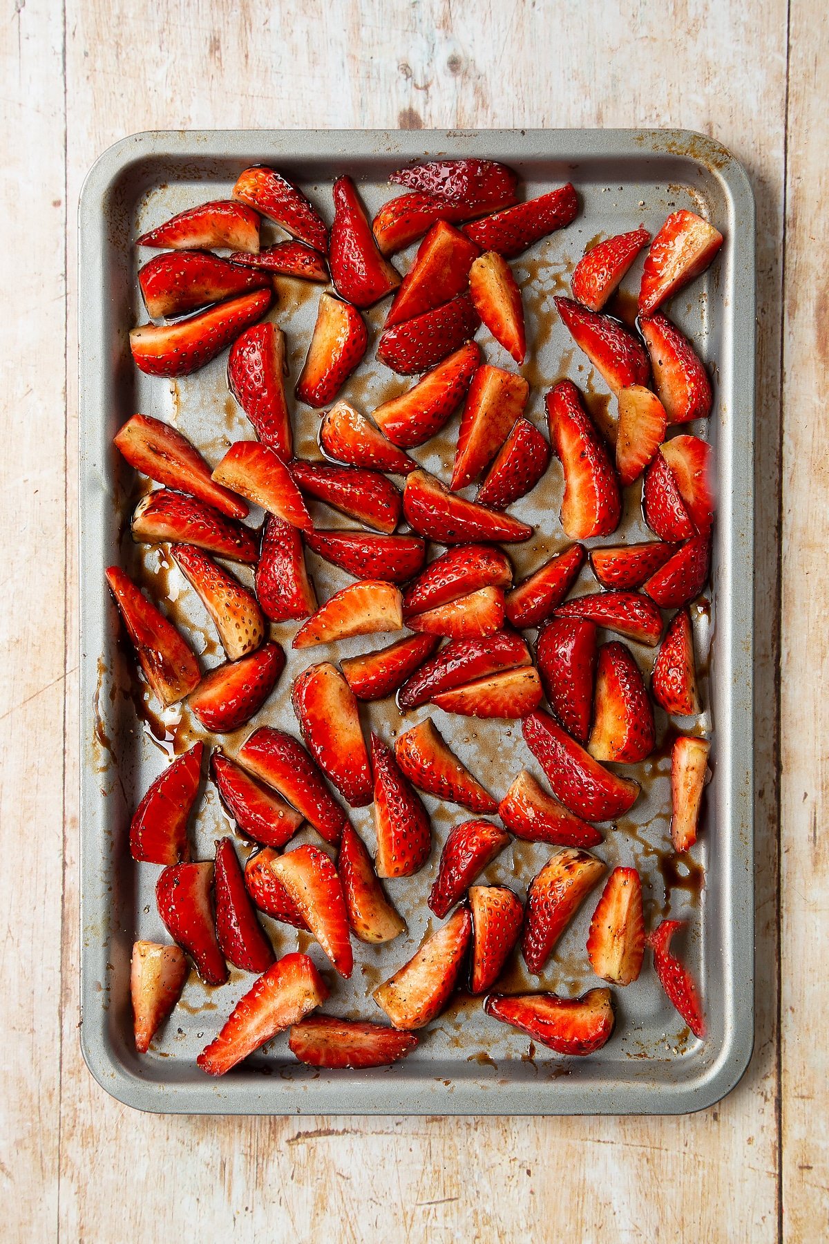 Strawberries sliced into quarters and mixed with pepper and balsamic glaze. placed on a non-stick tray.