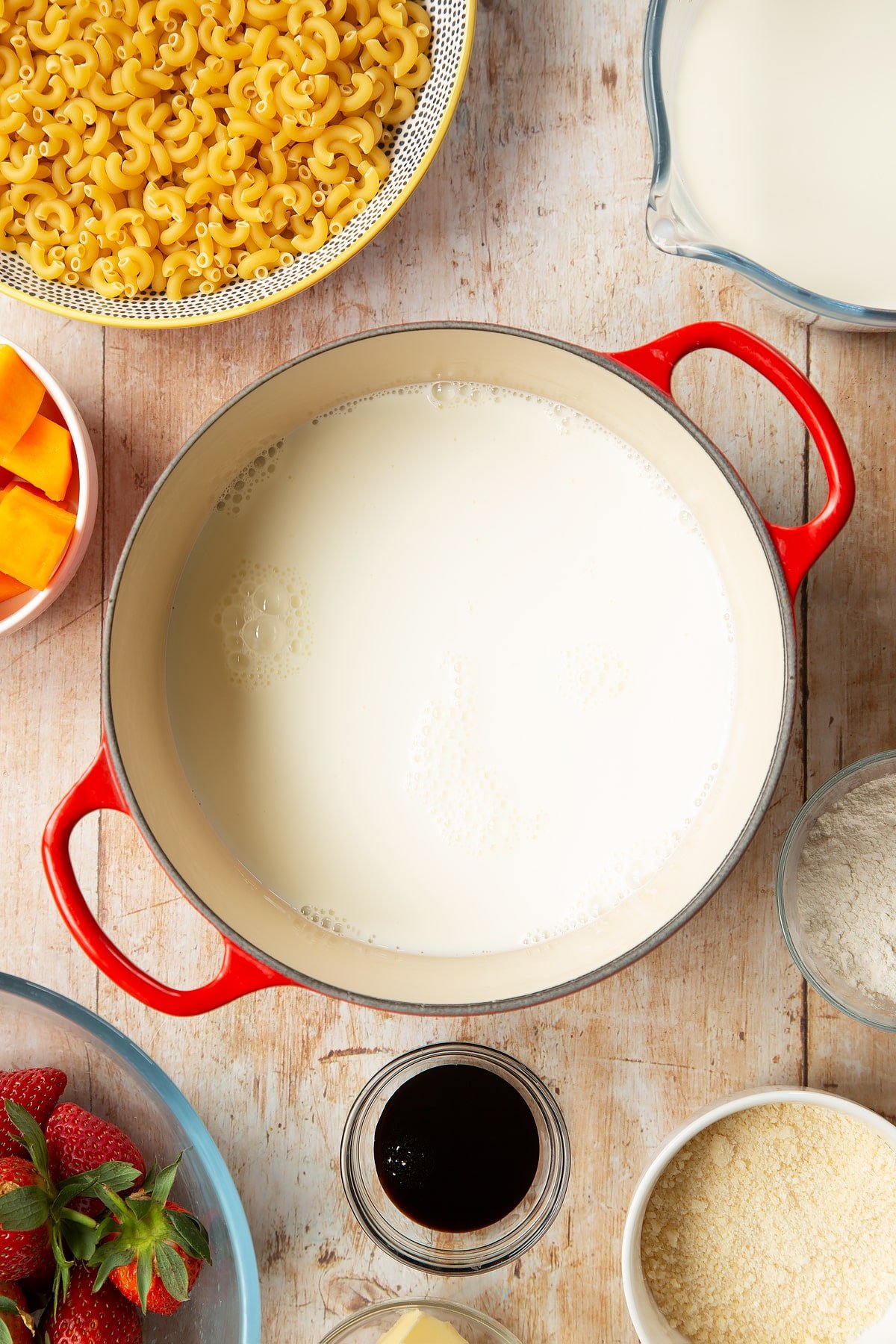 A saucepan containing milk. The pan is surrounded by ingredients for strawberry pasta. 