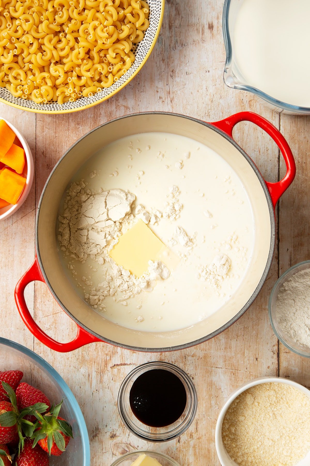 A saucepan containing milk, butter and flour. The pan is surrounded by ingredients for strawberry pasta. 