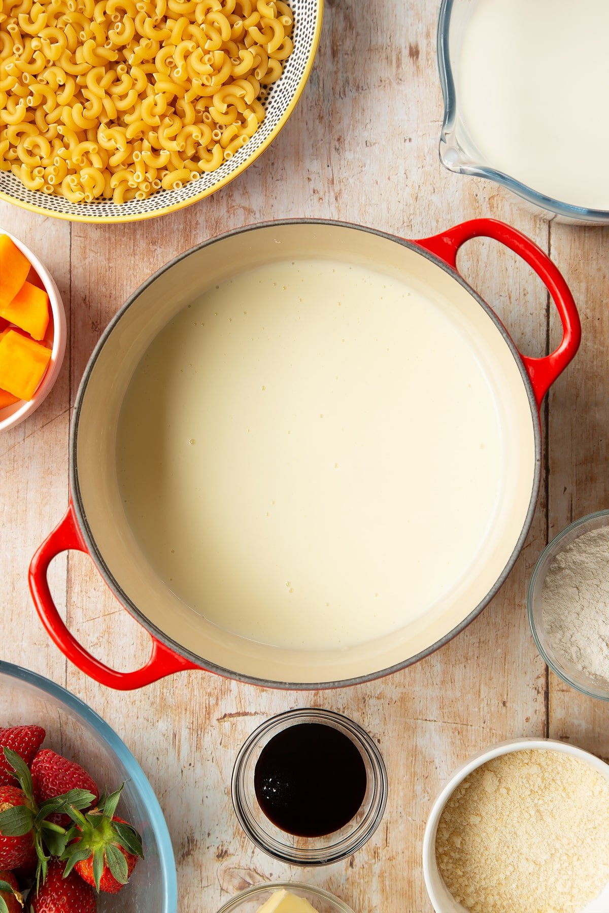 A saucepan containing a white sauce made with milk, butter and flour. The pan is surrounded by ingredients for strawberry pasta. 