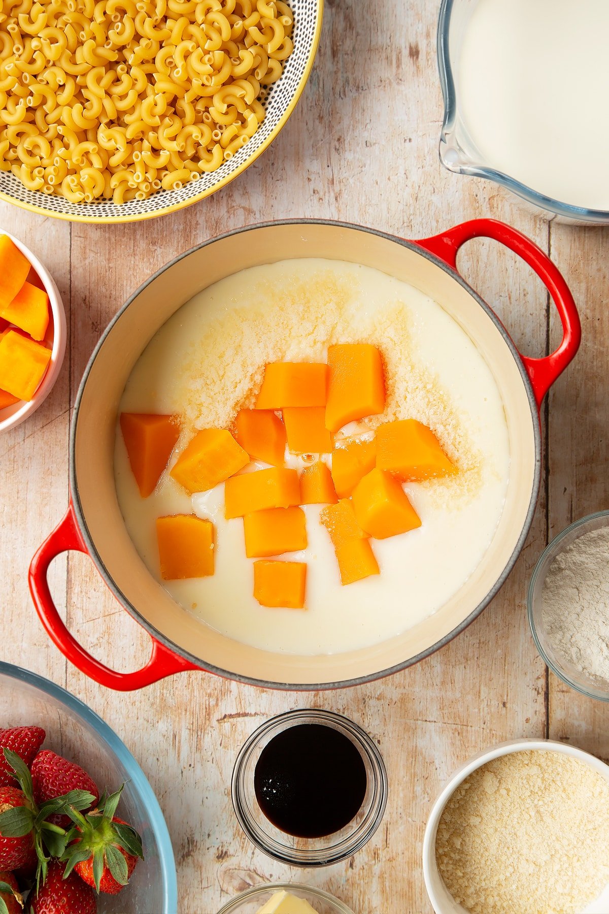 A saucepan containing a white sauce made with milk, butter and flour, topped with Parmesan cheese and butternut squash. The pan is surrounded by ingredients for strawberry pasta. 