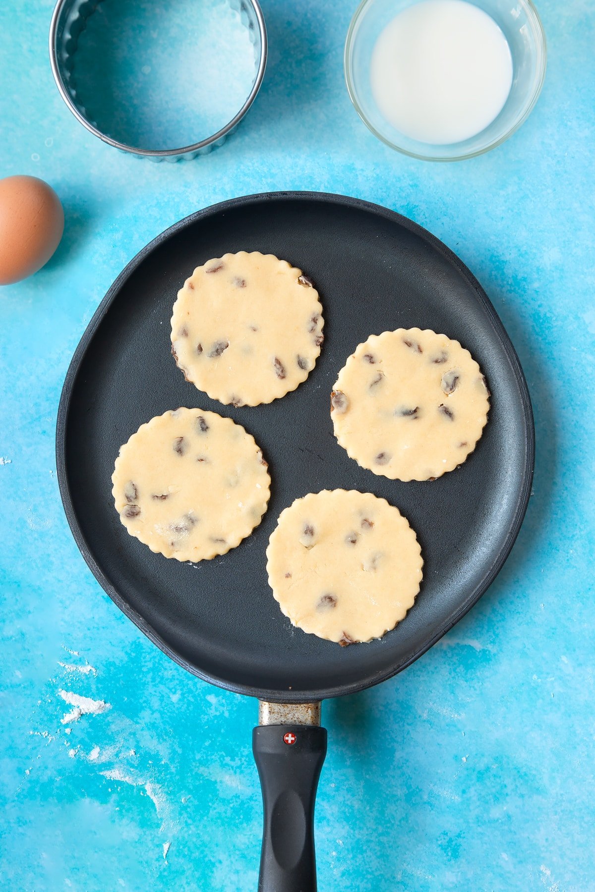 Welsh cake dough rounds cooking in a hot, flat pan.