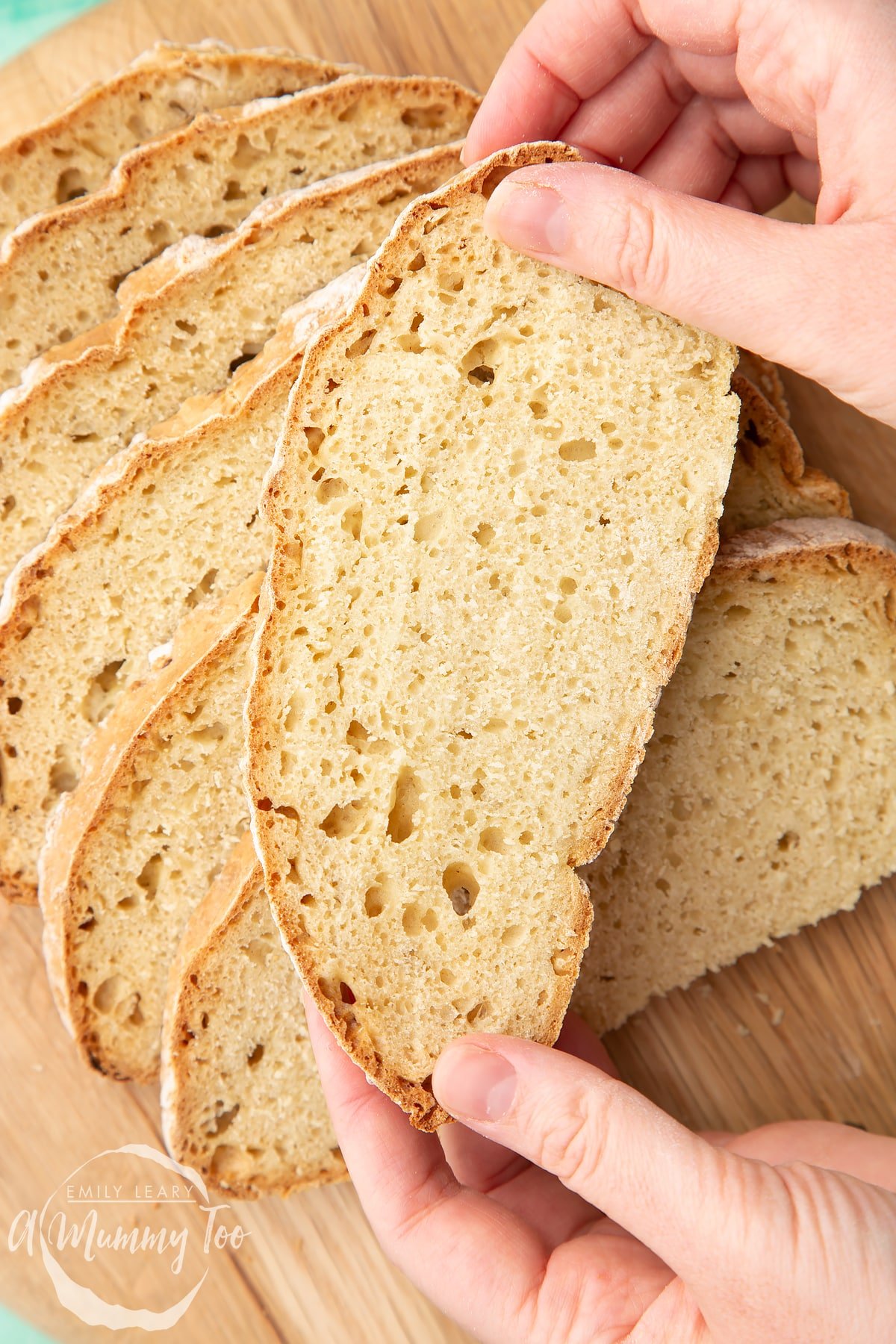 Close up of sliced soda bread without buttermilk on a wooden board. Hands hold a slice.