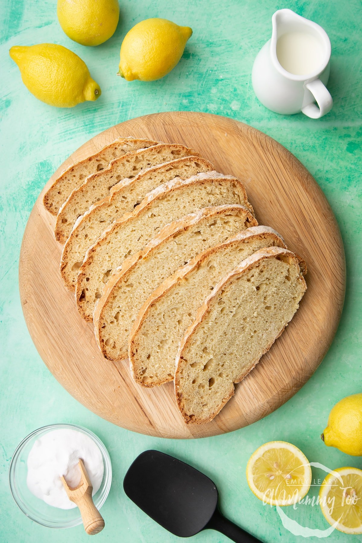 Sliced soda bread without buttermilk on a wooden board. Lemon, milk and bicarbonate of soda are placed around the board.