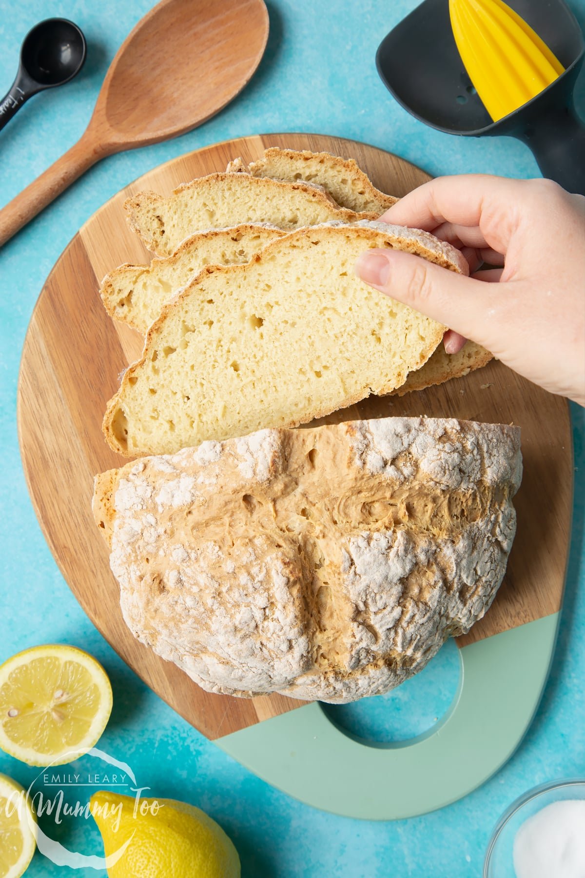 Vegan soda bread on a wooden board. Some of the bread has been cut into slices. A hand is taking a slice.