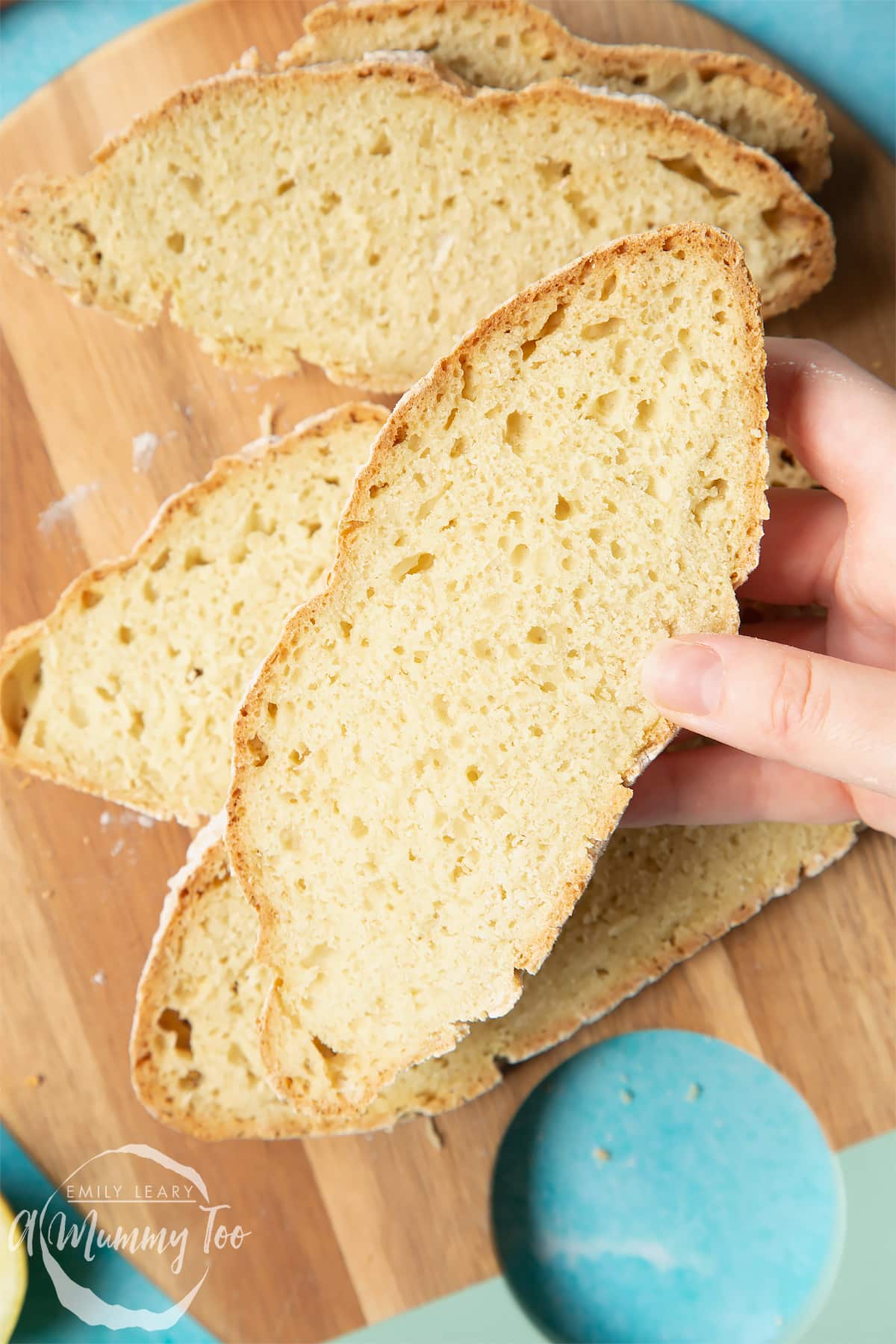 Vegan soda bread slices on a wooden board. A hand holds a slice.