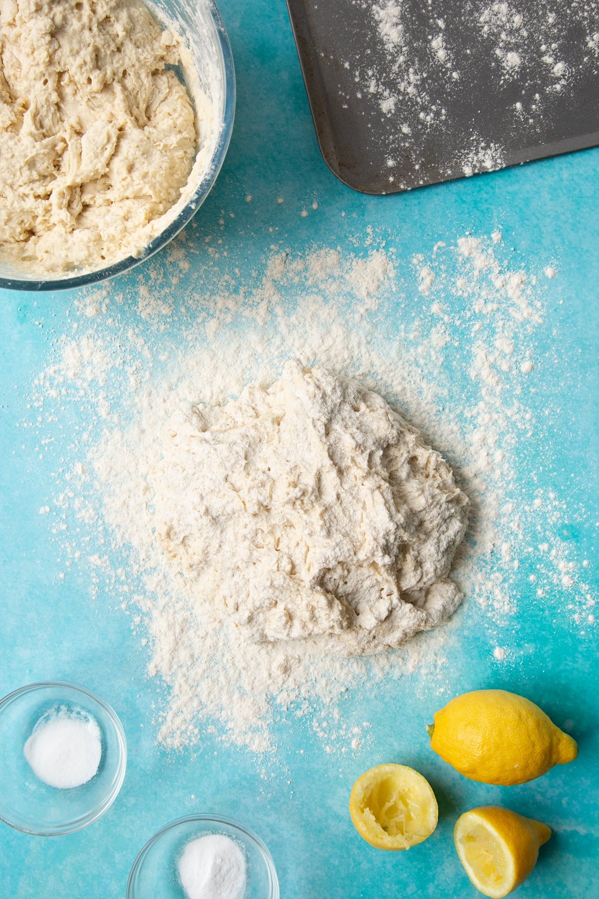 A wet dough on a floured surface, floured on top, surrounded by ingredients to make vegan soda bread.