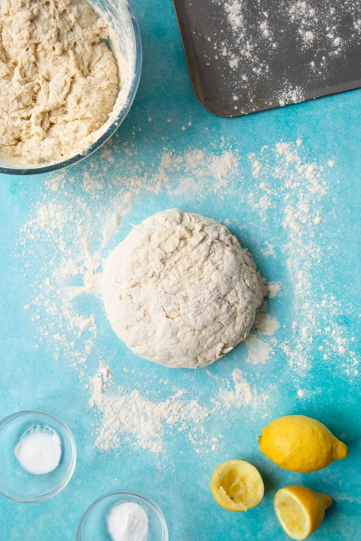 A shaped soda bread dough on a floured surface surrounded by ingredients to make vegan soda bread.