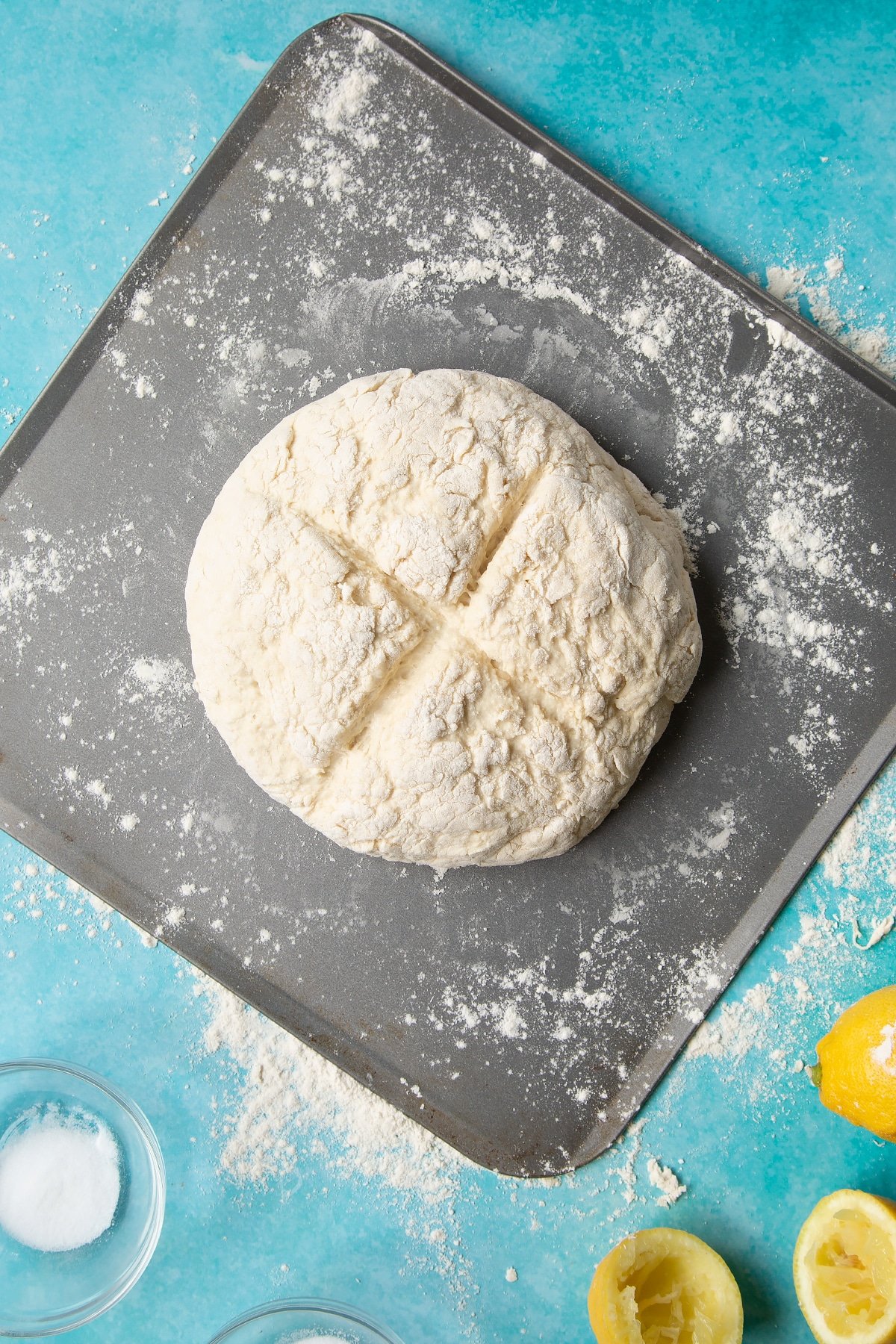 Vegan soda bread dough shaped into a round on a floured baking sheet, with an X scored into the top.
