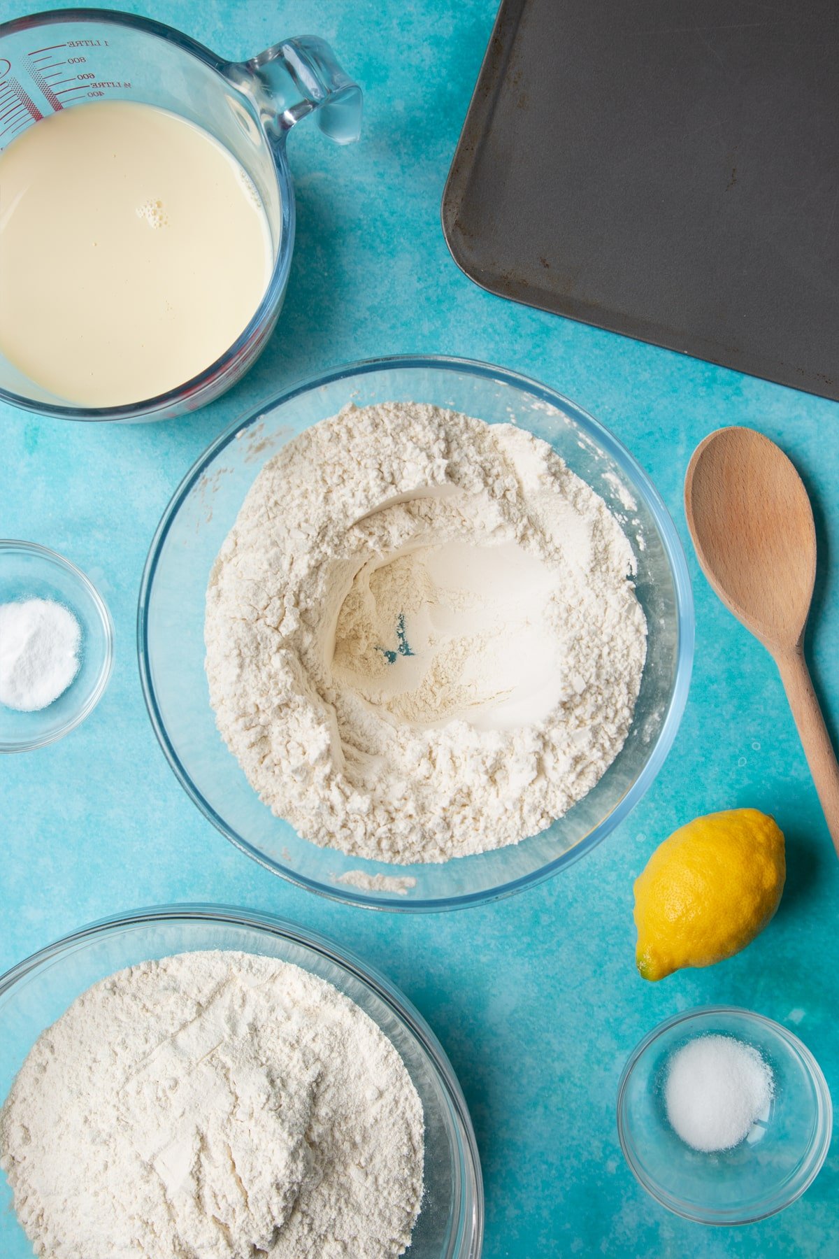 A bowl containing plain flour, salt and bicarbonate of soda, mixed with a well in the centre. Ingredients to make vegan soda bread surround the bowl.