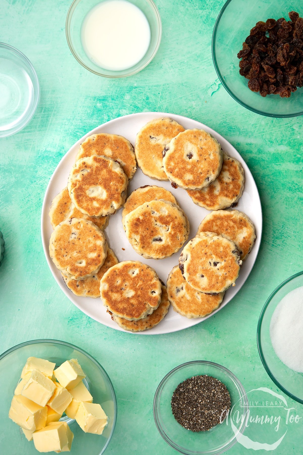 Vegan Welsh cakes arranged on a white plate. Surrounding the plate are ingredients to make them.