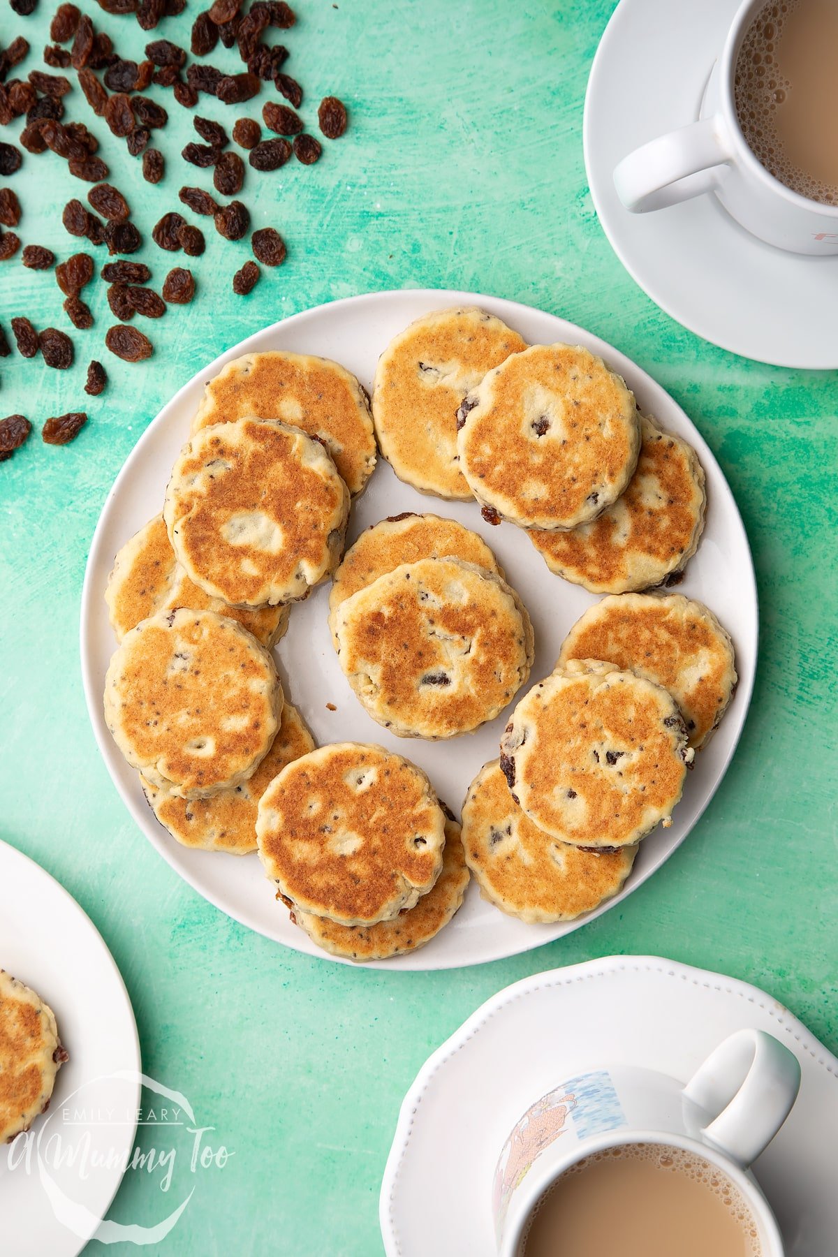 Vegan Welsh cakes arranged on a white plate. Surrounding the plate are cups of tea.