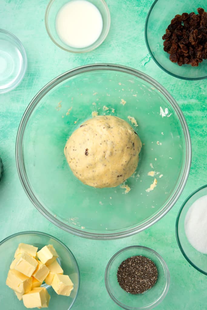 A glass mixing bowl containing vegan Welsh cakes dough. Ingredients to make vegan Welsh cakes surround the bowl.