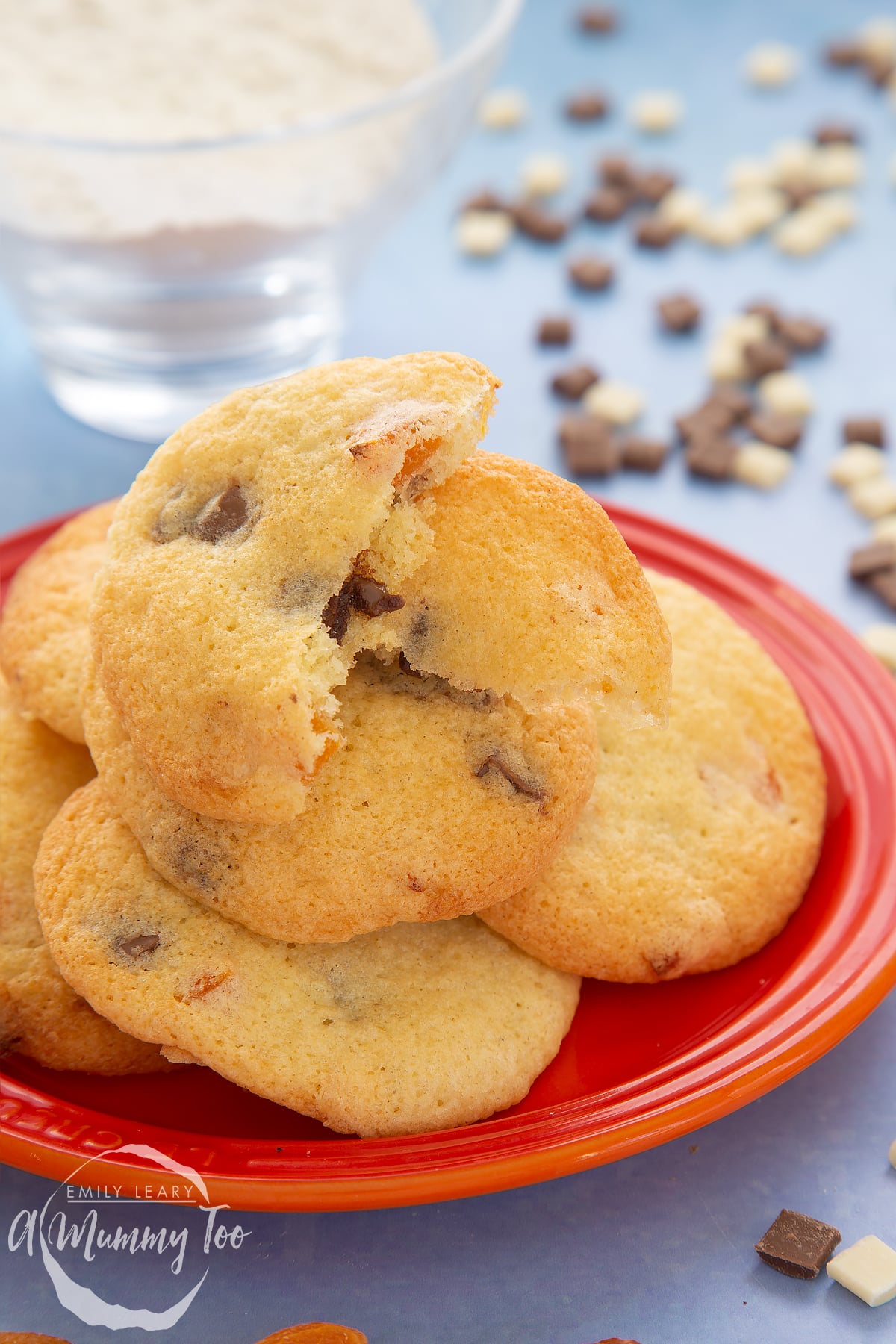 Apricot chocolate chip cookies stacked on an orange plate. The top cookie is broken in two.