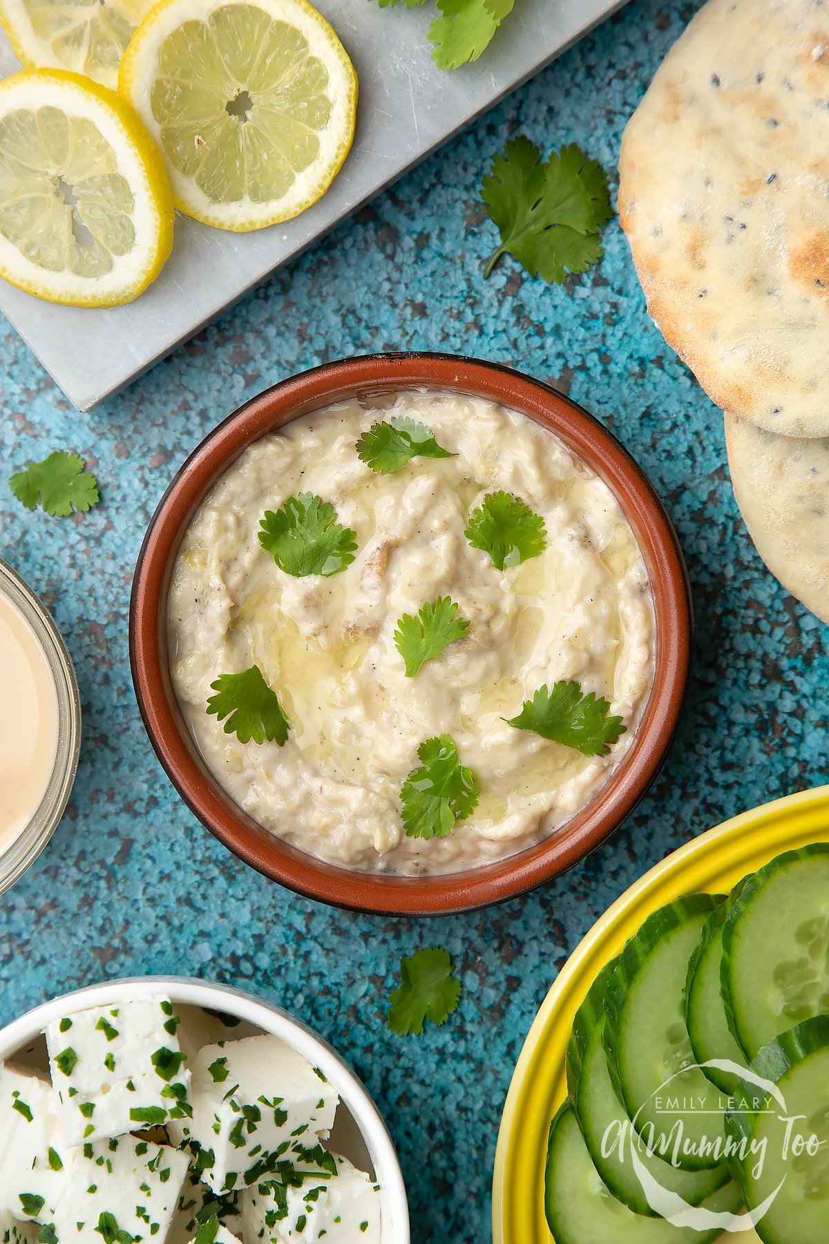 Baba ganoush in a small, shallow teracotta dish. The dip has been garnished with olive oil and parsley leaves.