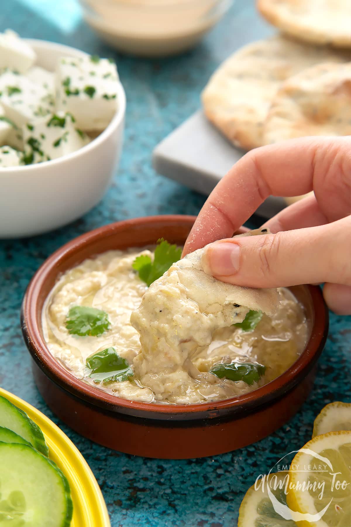 Baba ganoush in a shallow terracotta dish. A hand dips flat bread into the dish.