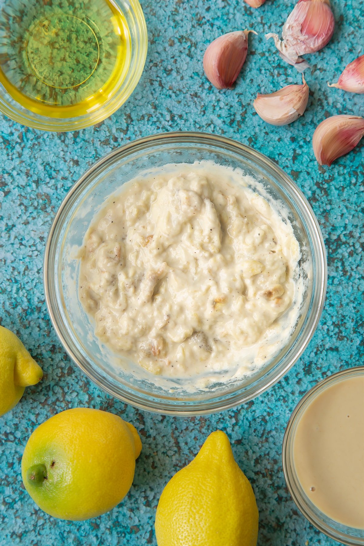 Baba ganoush in a small glass bowl. Ingredients to make an easy baba ganoush recipe surround the bowl. 