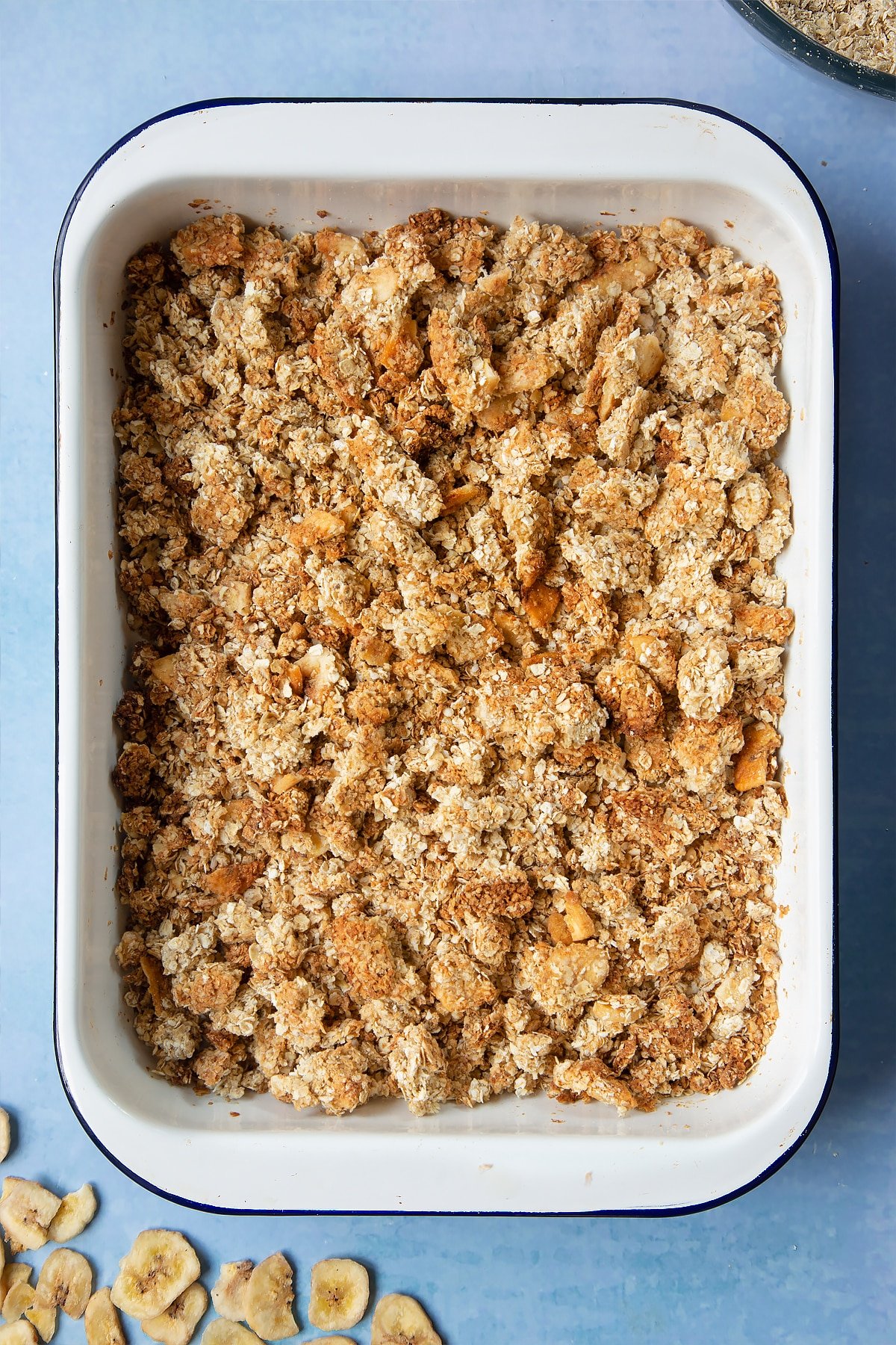 A white, medium-sized roasting tray filled with crumbled banana coconut granola.