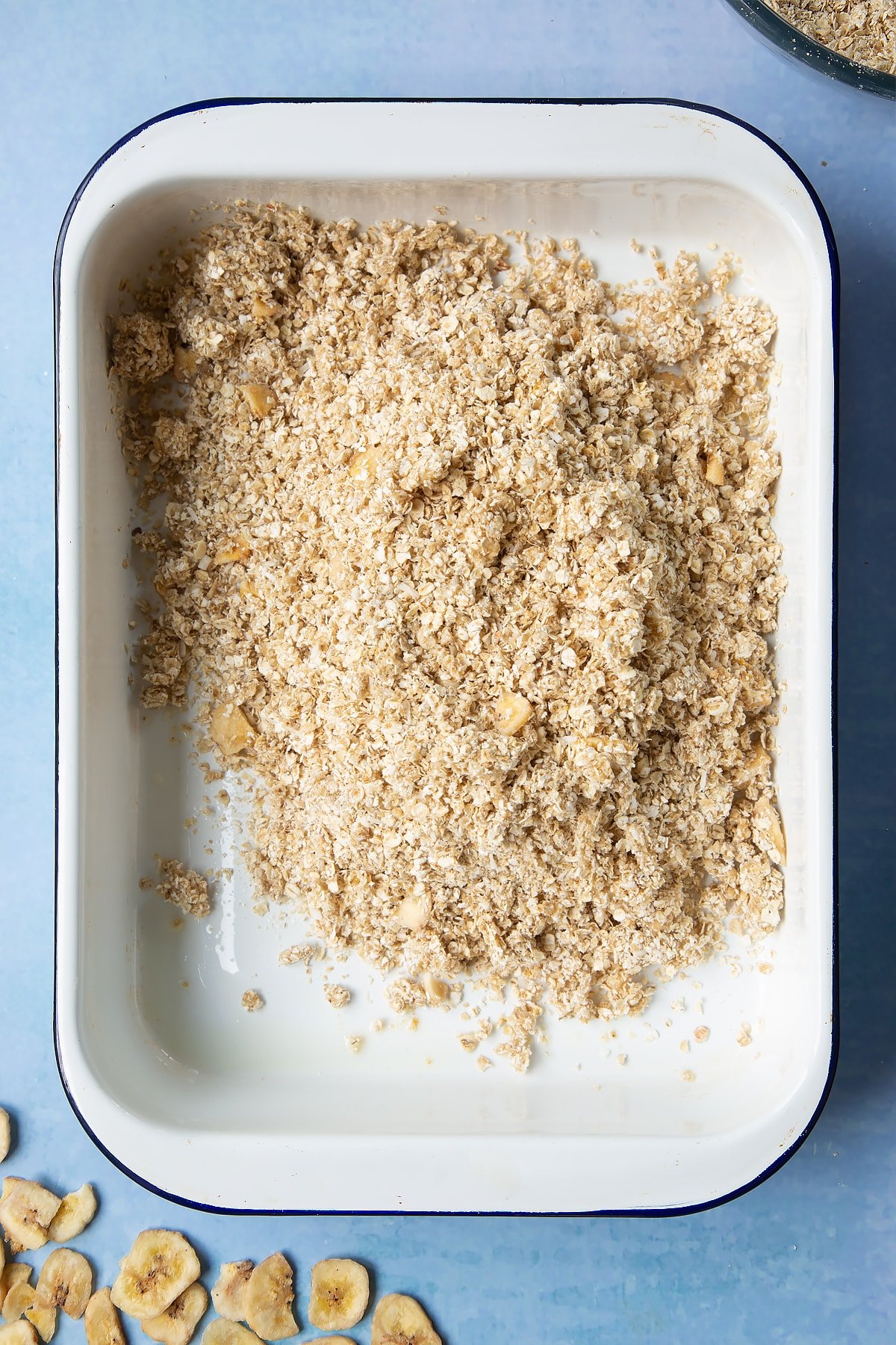 A white, medium-sized roasting tray with banana coconut granola mix tipped into it.