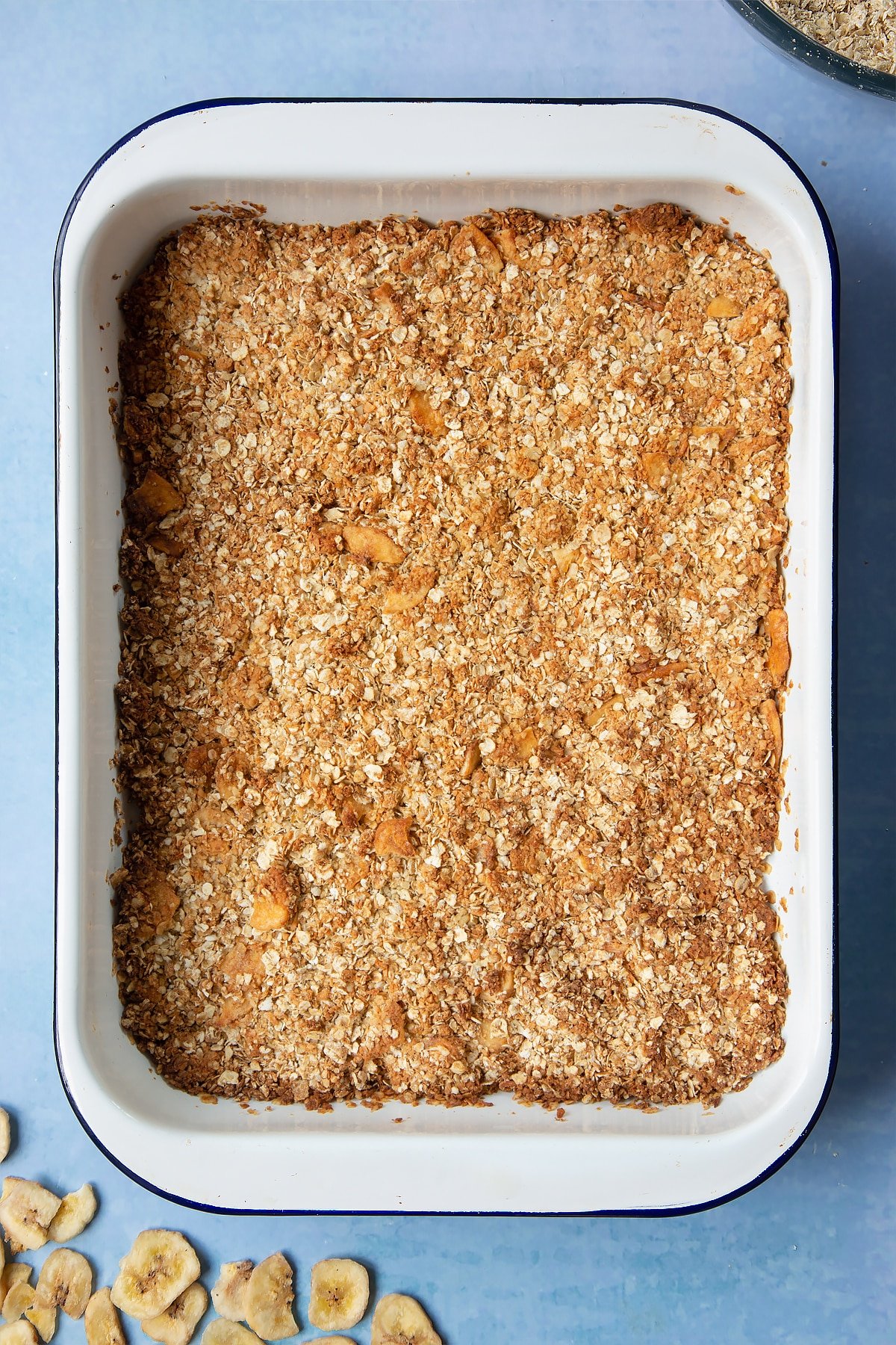 A white, medium-sized roasting tray filled with freshly baked banana coconut granola.