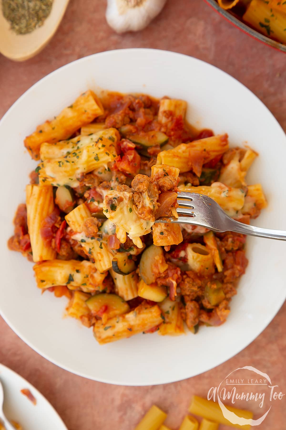 Close up of bolognese al forno on a fork, with more on a plate in the background. 