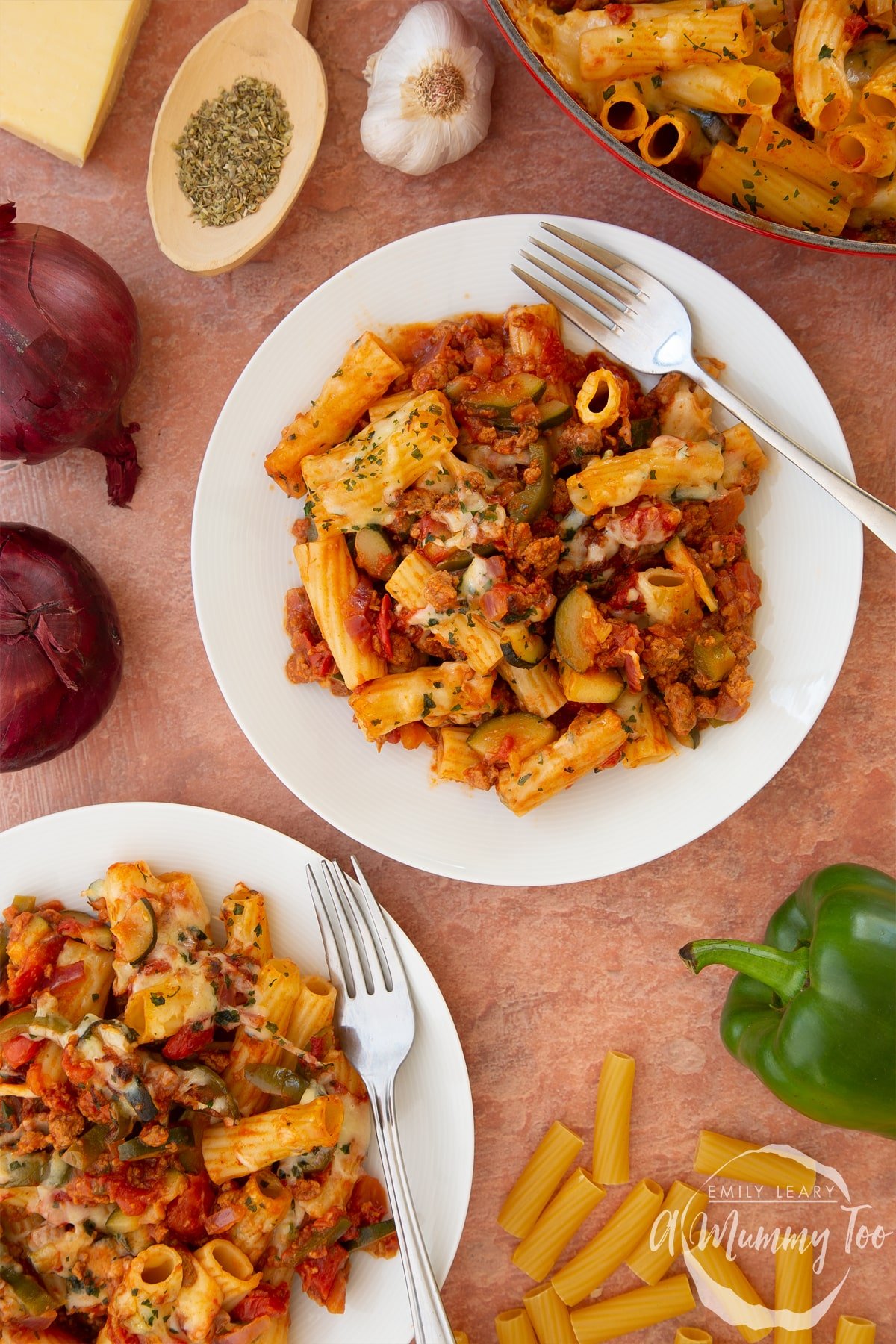 Bolognese al forno served onto two white plates with forks. Ingredients surround the plates.