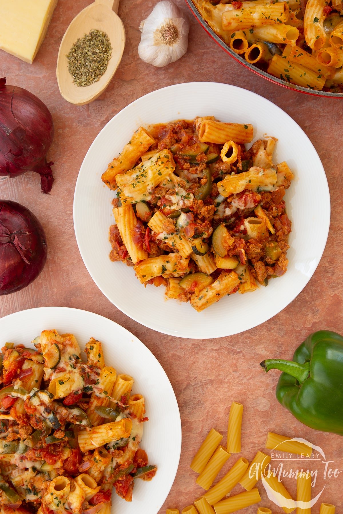 Bolognese al forno served onto two white plates. Ingredients surround the plates.