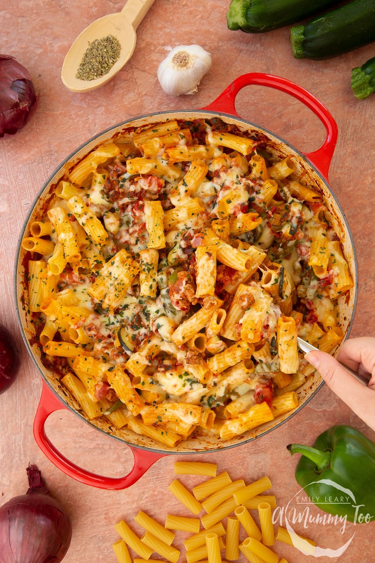 A casserole dish containing freshly baked bolognese al forno. A hand digs a large serving spoon into the dish.