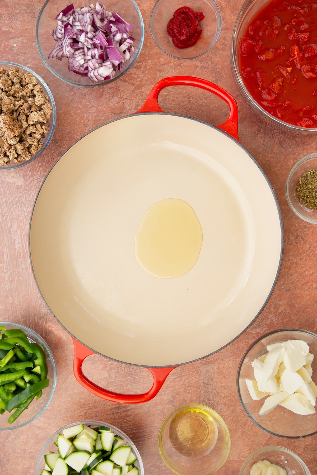 A casserole dish containing a little oil. Ingredients to make bolognese al forno surround the dish.