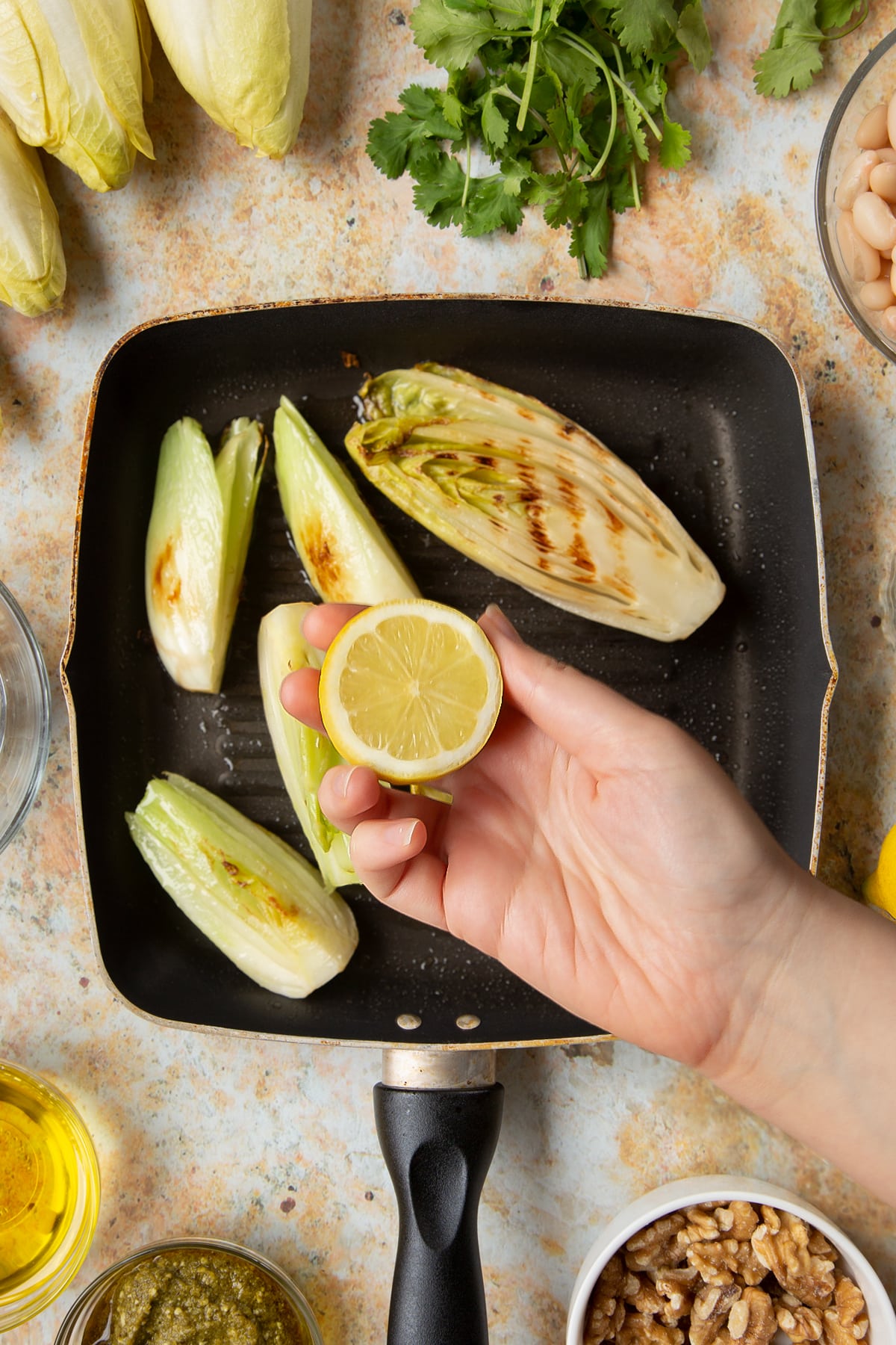 Chicory and fennel in a griddle pan. A hand holds a lemon above.