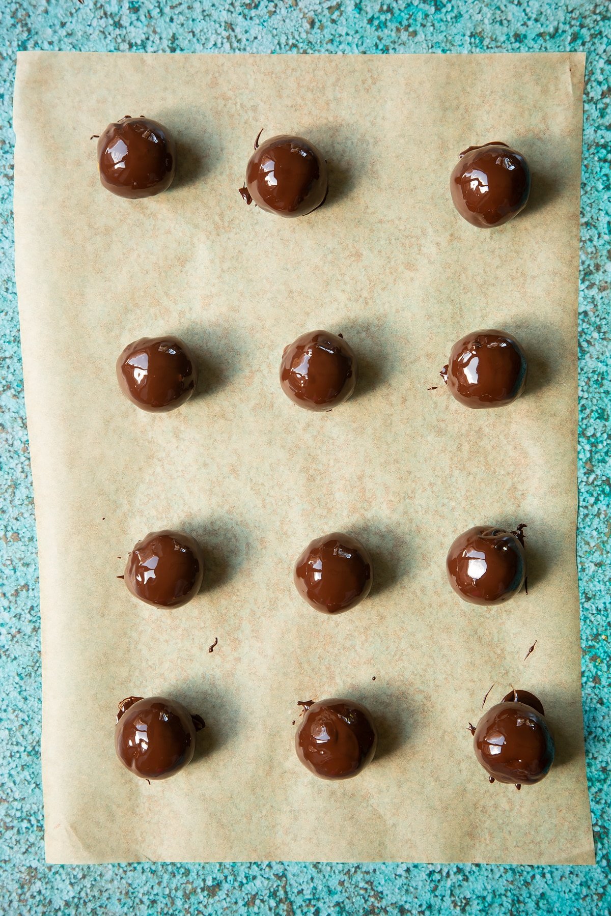 12 apricot balls coated in melted chocolate. The balls are on a piece of baking paper.