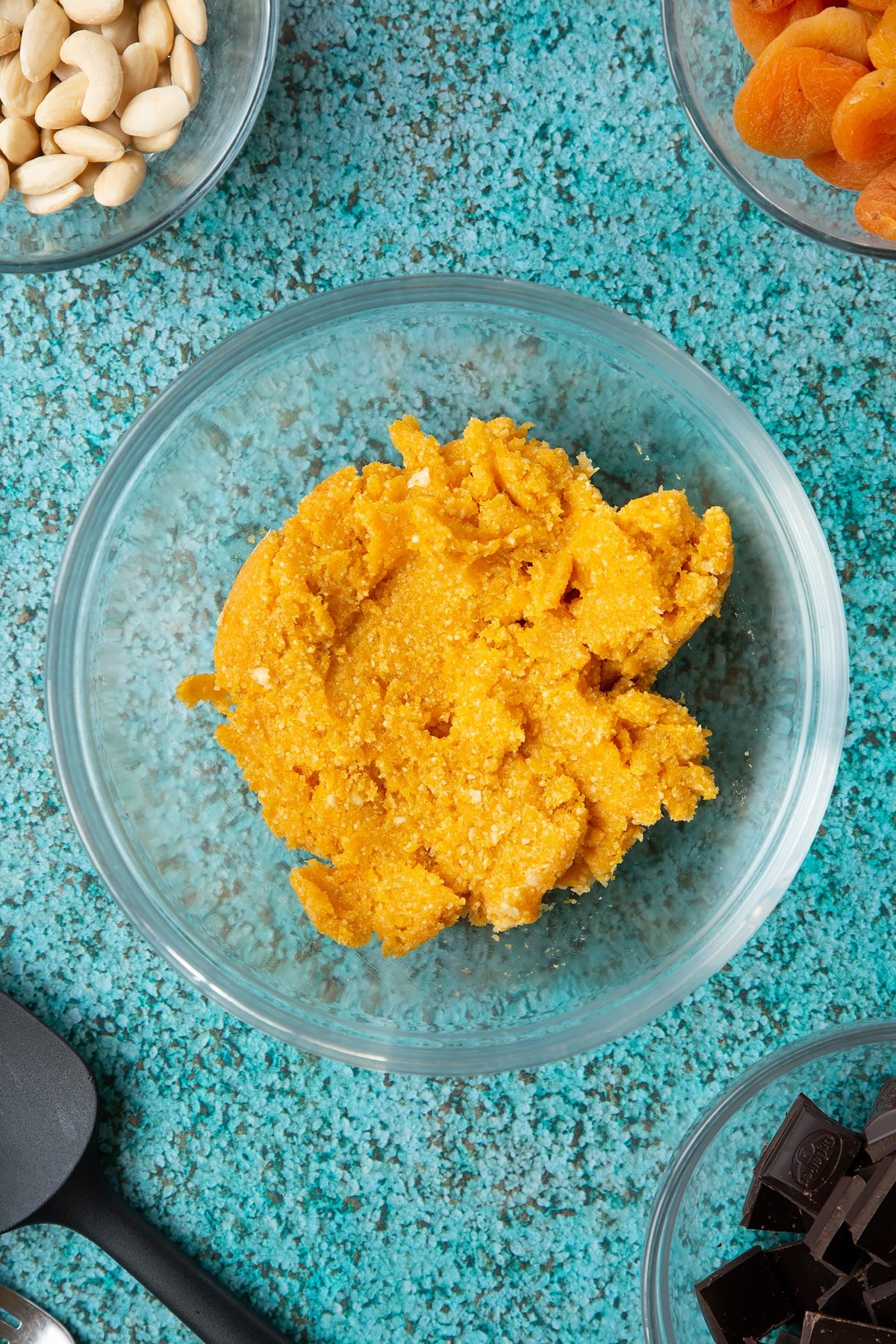 A bowl containing almonds, apricots and a few cashews blitzed together to a paste. Ingredients to make chocolate apricot balls surround the bowl.