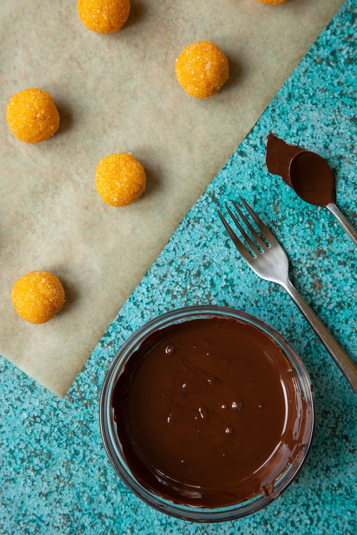 Balls made from blended, apricots and nuts. A small mixing bowl containing melted dark chocolate.