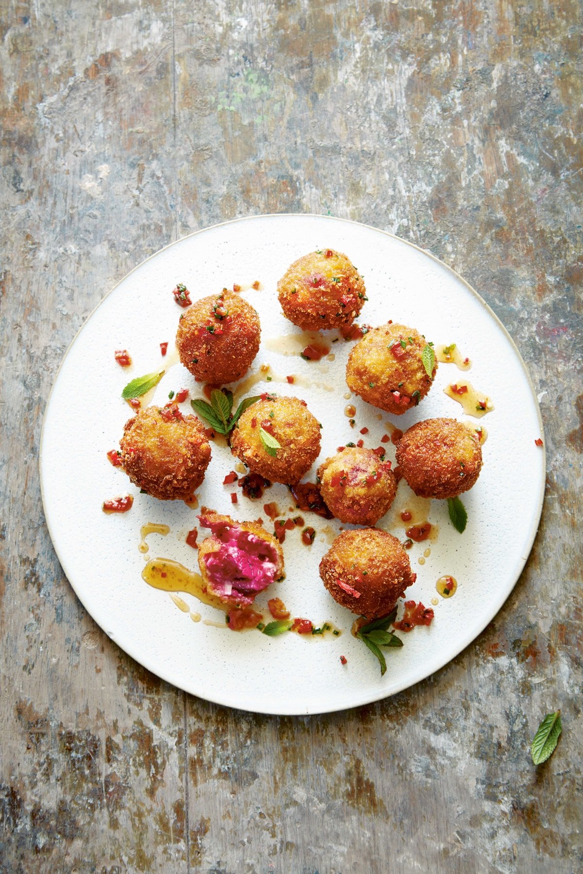Goat's cheese croquettes on a large white plate. They have been dressed with maple syrup, red chilli, chives and mint.