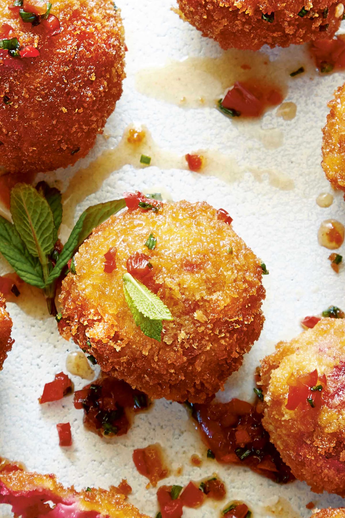 Close up of a goat's cheese croquette. The croquettes have been drizzled with maple syrup, red chilli and chive dressing and garnished with mint. 