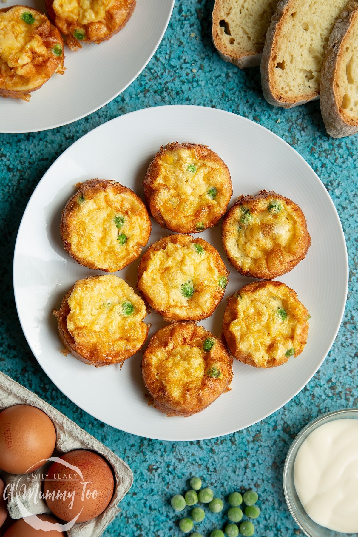 Mini vegetable frittatas arranged on a white plate. Slices of bread and ingredients surround the plate.