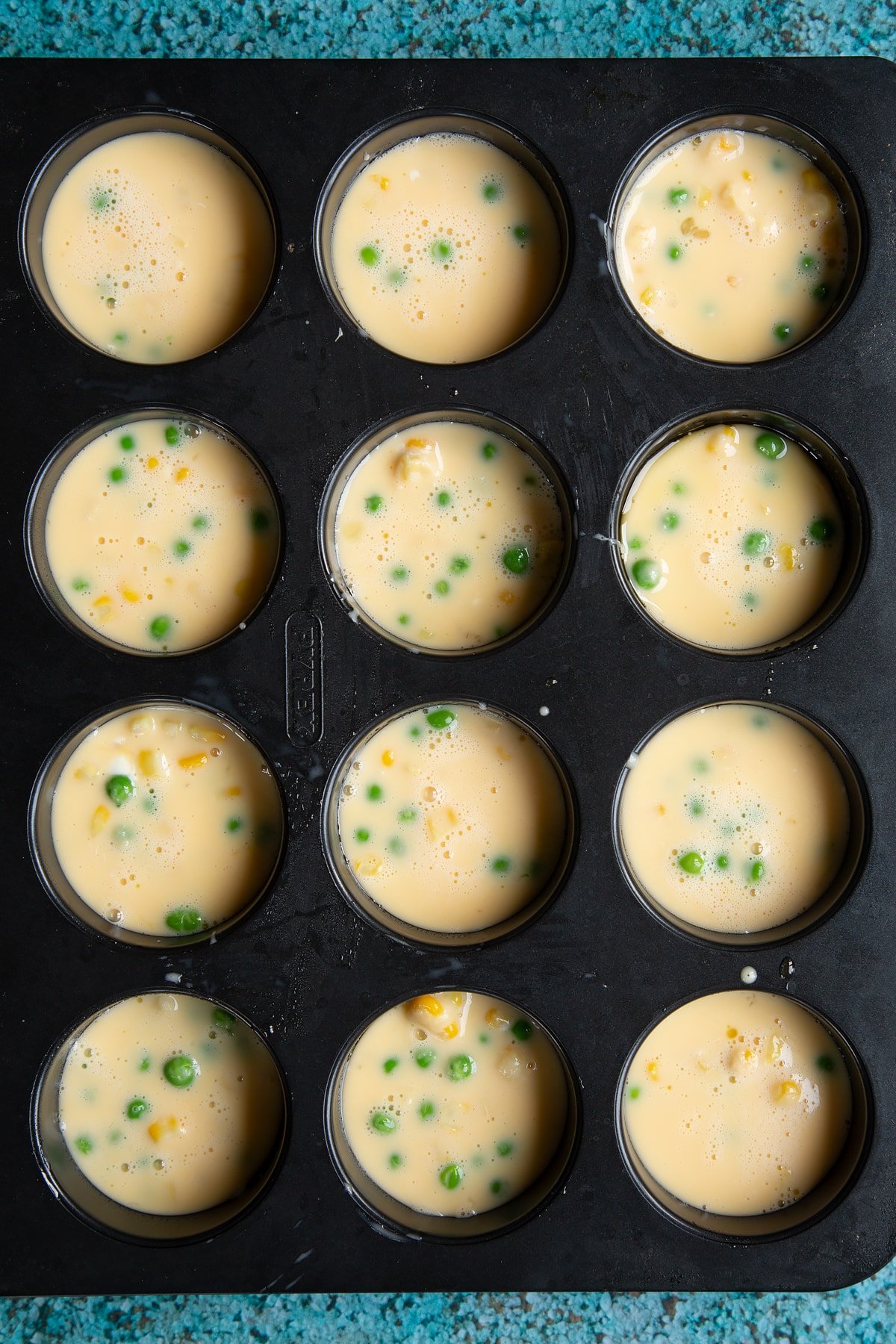 An oiled muffin tray filled with egg mix to make mini vegetable frittatas.