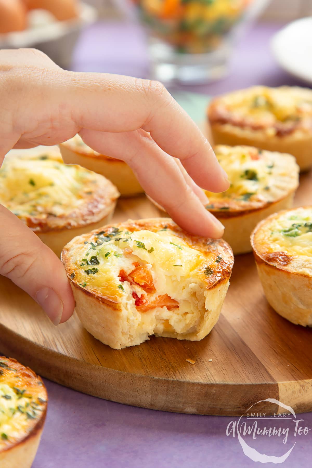 A hand reaching for a mini vegetable quiche on a wooden board. 