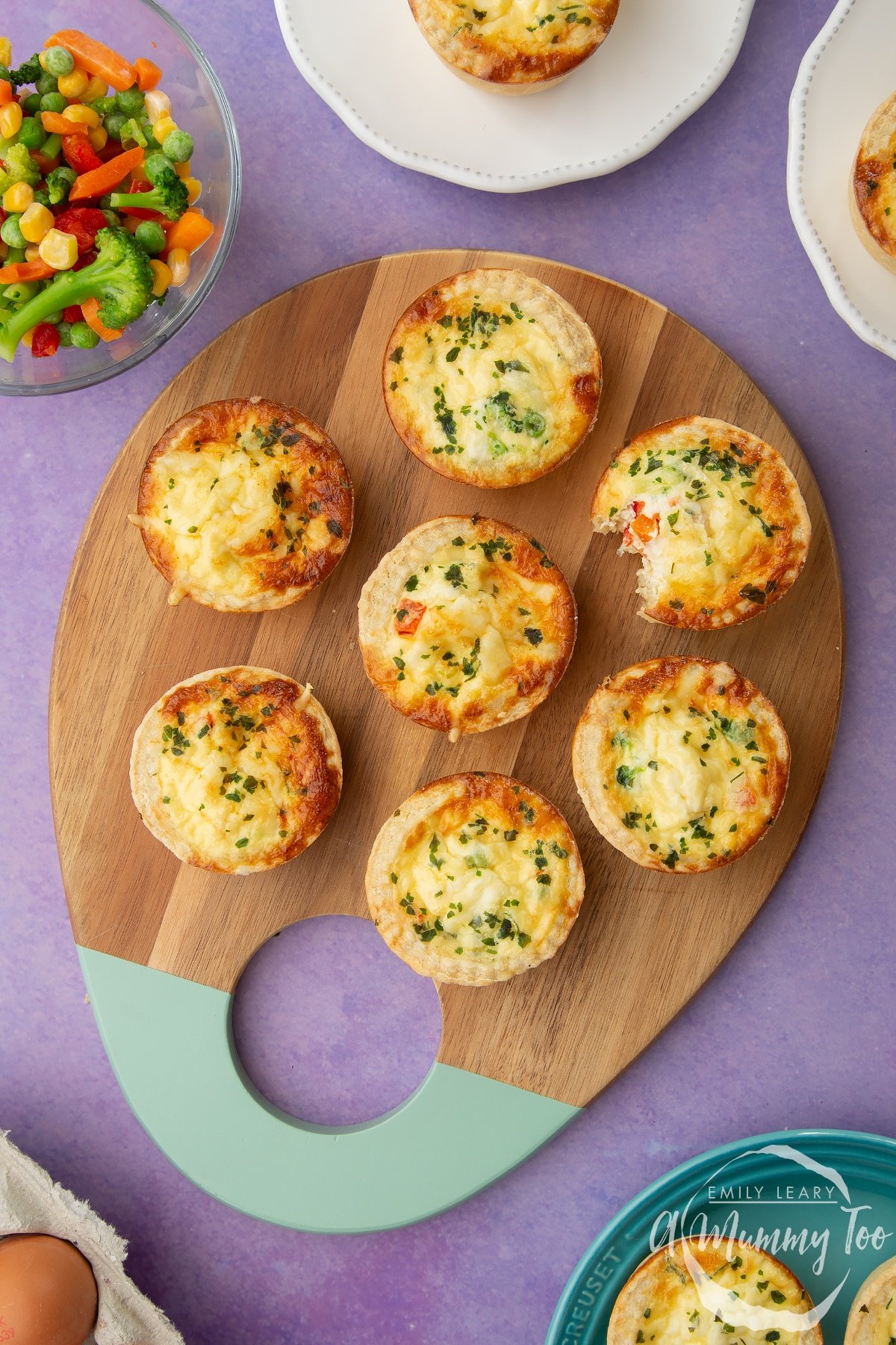 Mini vegetable quiches arranged on a wooden board. A bite has been taken out of one.