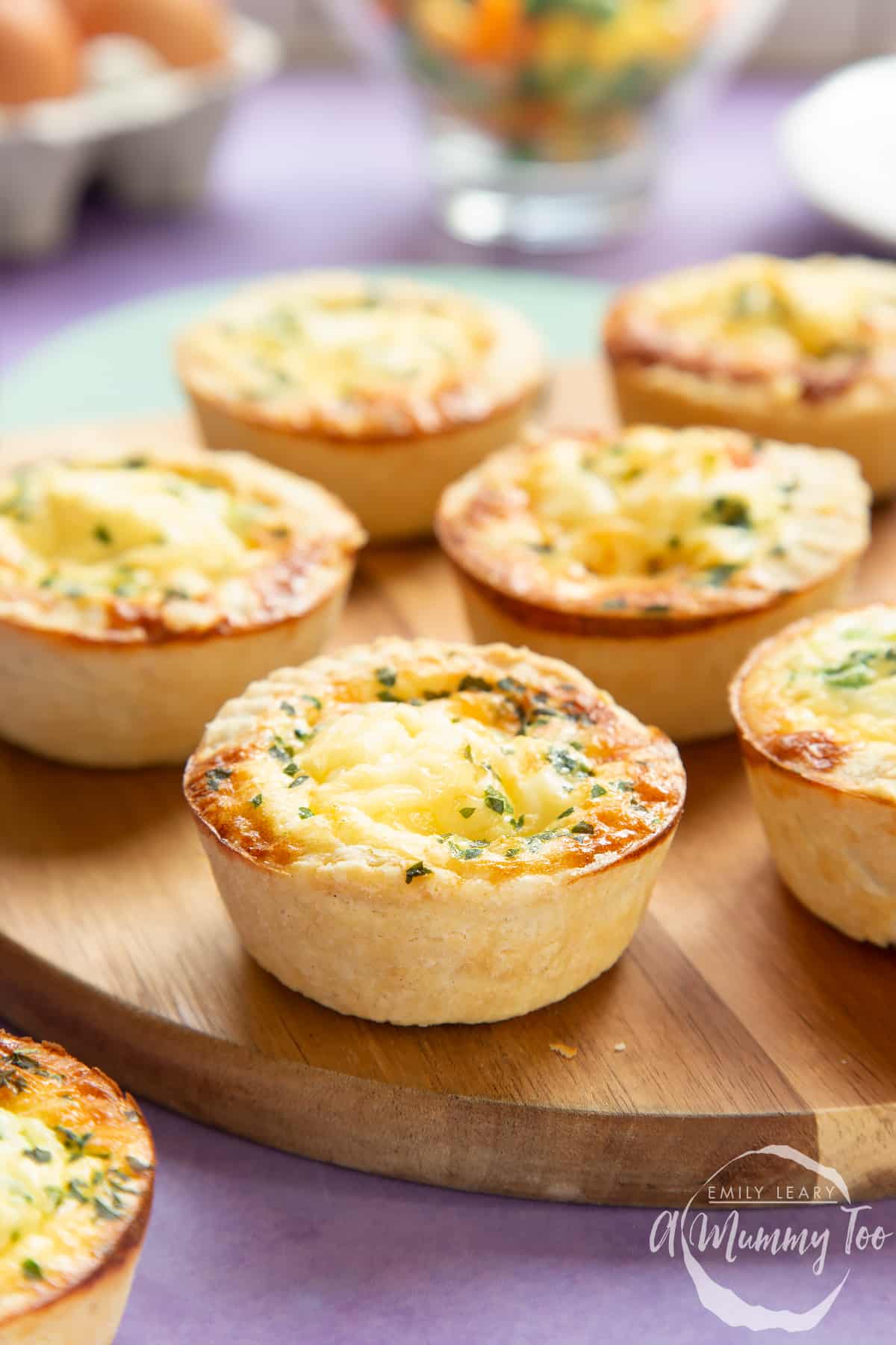 Mini vegetable quiches on a wooden board with ingredients in the background.