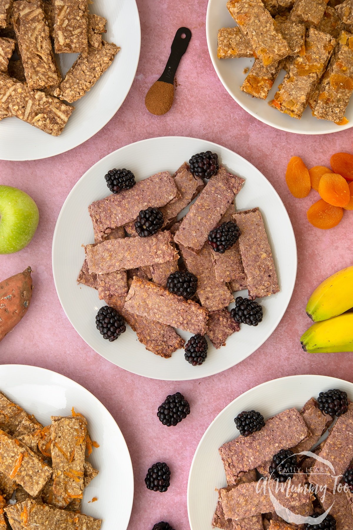 White plate piled with blackberry oat fingers. Other flavours of oat fingers sit on plates around the edge of the frame.