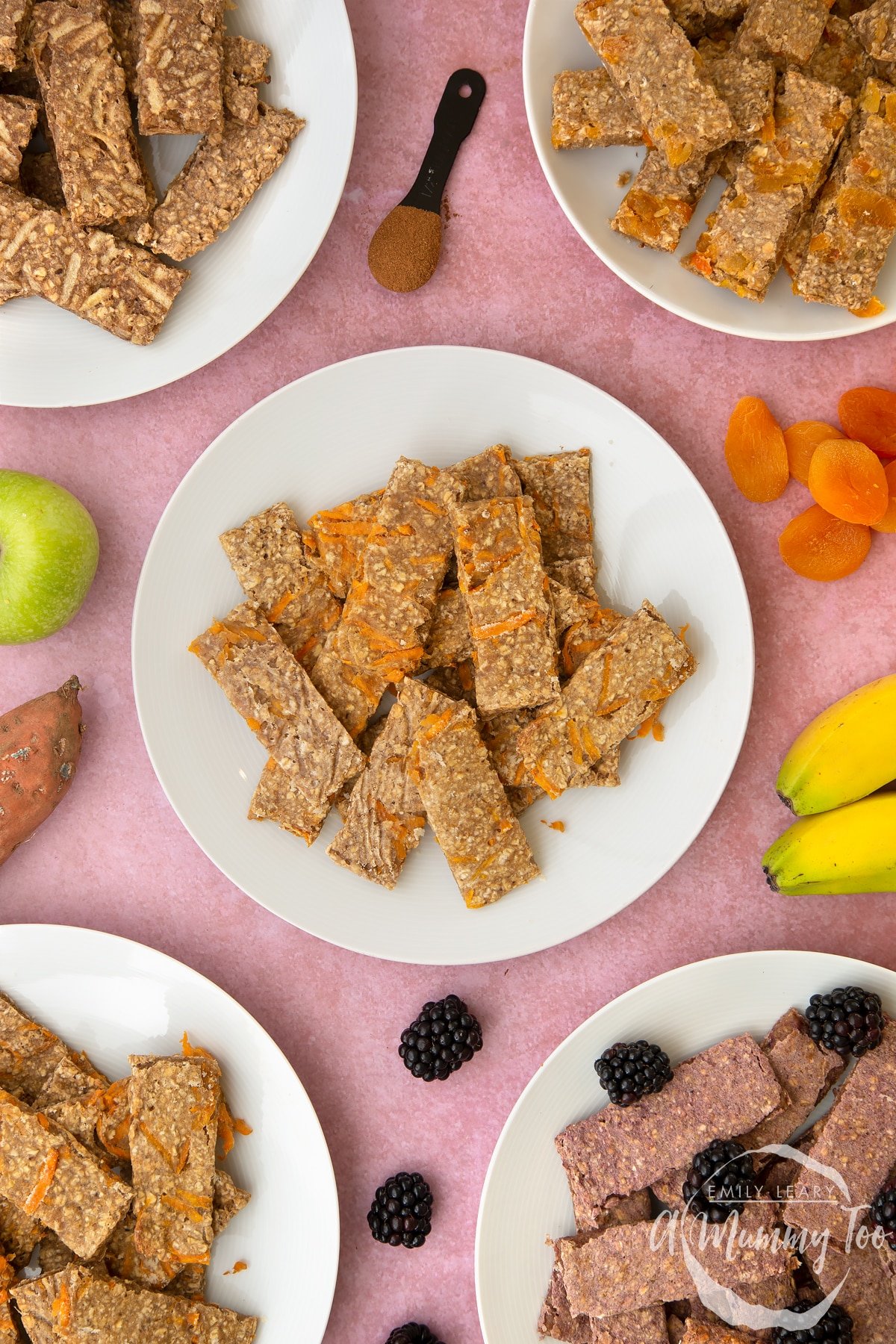 White plate piled with sweet potato oat fingers. Other flavours of oat fingers sit on plates around the edge of the frame.