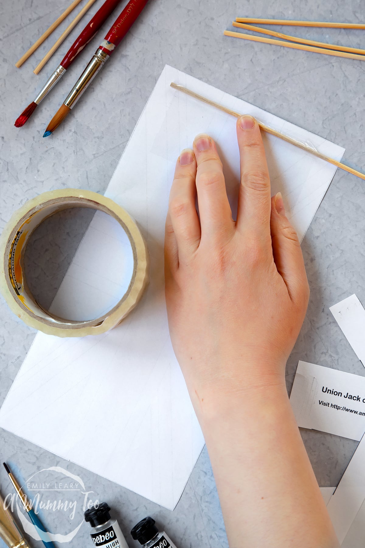 a hand holding down the wooden dowl to the paper union jack.