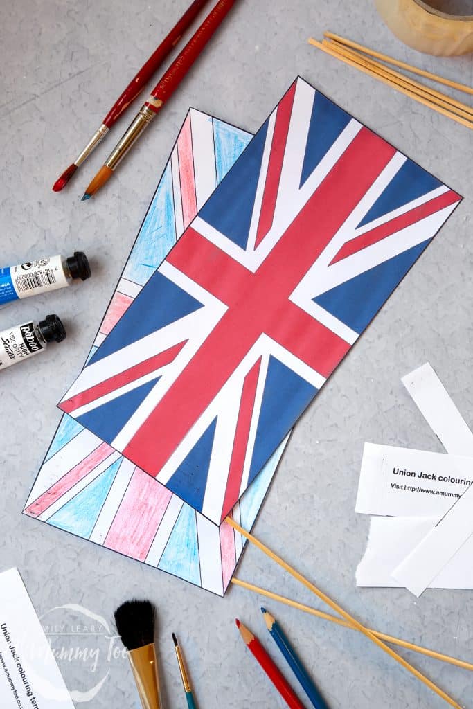 two paper union jack flags with sticks surrounded by paintbrishes, coloured pencils and paper.