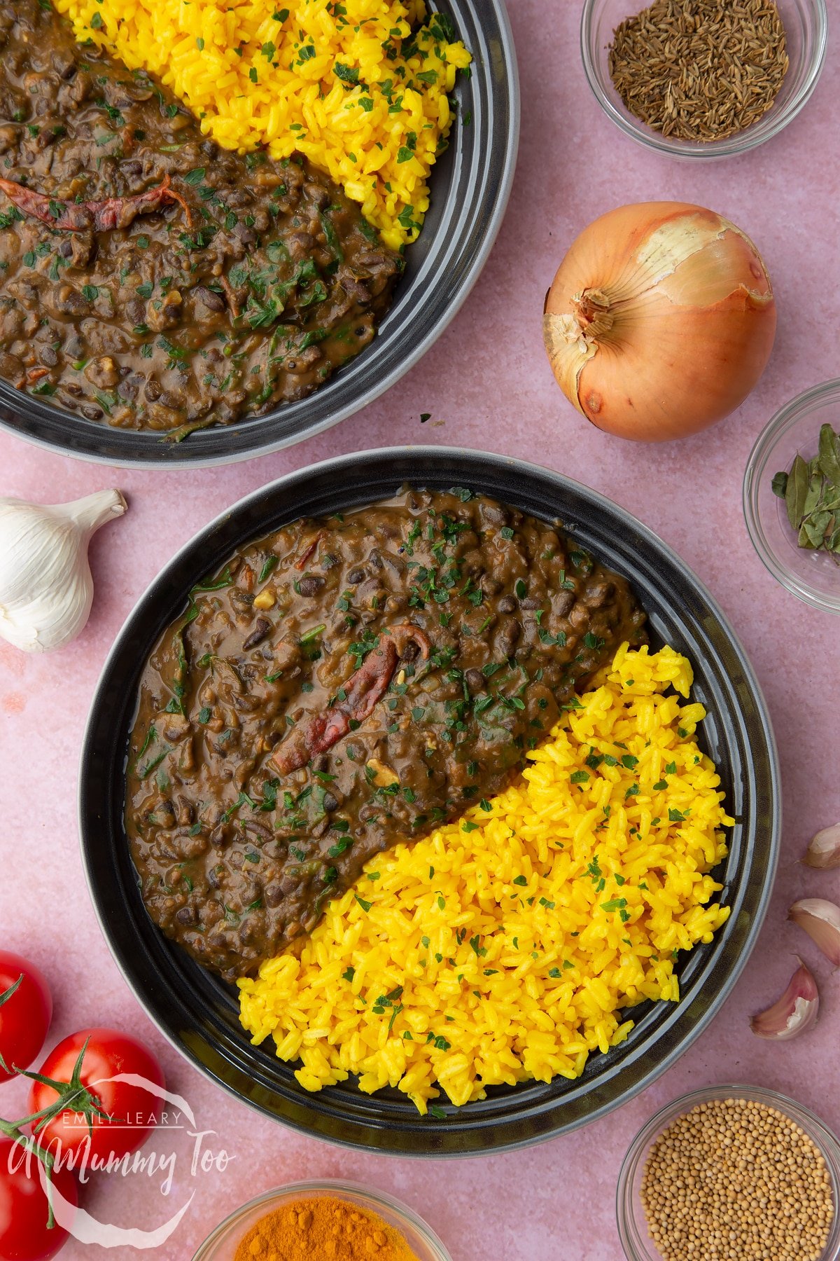 Black bean curry served to two shallow grey bowls with yellow rice.