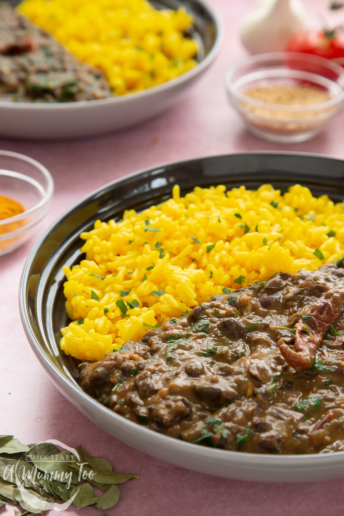 Black bean curry served to a shallow grey bowl with yellow rice.